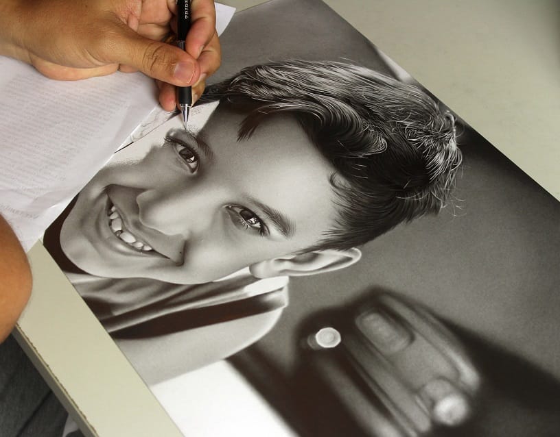 Desenhista trabalhando em um retrato realista sobre a mesa, com foto de referência ao lado
